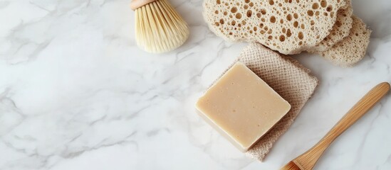 Poster - Beige soap bar placed on a soap saver bag alongside a natural sponge and brush on white marble top view copy space Herbal product for facial and body care