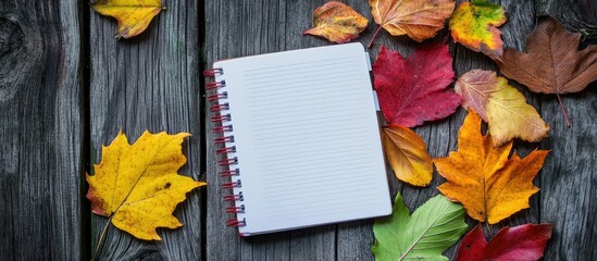 Poster - Autumn leaves alongside a notebook on a wooden surface top view. with copy space image. Place for adding text or design