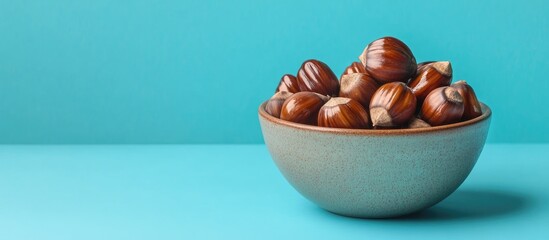 Poster - A square photo featuring both peeled and unpeeled roasted chestnuts in an earthenware bowl set against a bright teal blue background. with copy space image. Place for adding text or design
