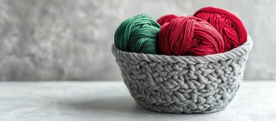 Poster - Green and red yarn in a gray knitted basket on a white table Concept of home comfort and Christmas Knitting as a hobby for both women and men. with copy space image. Place for adding text or design