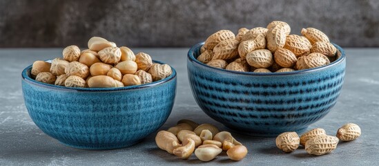 Aufkleber - Two blue ceramic bowls contain nuts One bowl has peanuts in their shells while the other holds peeled nuts Beside the bowls are peeled peanut kernels set against a gray background Closeup