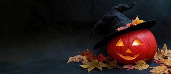 Poster - large pumpkin for Halloween black witch hat adorned with autumn golden leaves against a black background. with copy space image. Place for adding text or design