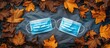 © vxnaghiyev - Autumn flat lay arrangement featuring protective masks and dried leaves Two blue medical masks on a gray backdrop surrounded by the leaves Concept of autumn quarantine time. with copy space image