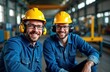 © miss irine - Two smiling industrial workers wear safety gear in factory. Wearing hard hats, ear protection. Appear focused on job. Manufacturing workers in plant workshop. Metal cutting machine in background.