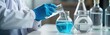 © miss irine - Scientist in lab coat wearing gloves pours liquid from flask into glass beaker. Analysis of blue solution. Research in progress. Closeup view of chemistry lab scene. Pro chemist handling chemicals.