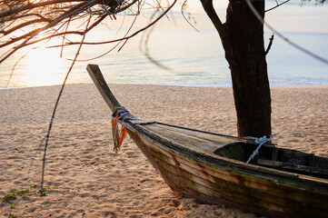 Sticker - A traditional wooden boat on a sandy beach at sunset, with the ocean and sky in the background.