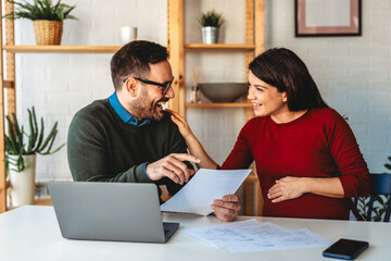 Wall Mural - Happy pregnant wife, woman with husband making online payment using laptop at home.