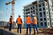© miss irine - Construction engineers, managers discuss project plan on building site. Team looks at new construction project. Men in safety vests, hard hats review blueprints. Sunny day at work site. Real estate