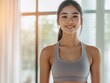 © The 2R Artificiality - Young Asian woman in gray sports bra smiling during indoor exercise session with bright natural light and large empty space for text.