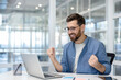 © Liubomir - Man celebrating victory inside office at workplace, businessman working with laptop joyfully holding hands up, satisfied received excellent results achievement.