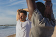© Ana BG - Two men, one Caucasian and one Black, stretching together before a workout on the beach at sunset