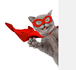 Aufkleber - Happy cat wearing superhero costume looking above from behind blank white banner and waves his paw. Isolated on white background.