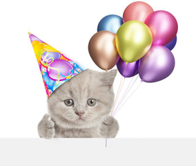 Fototapete - Funny kitten wearing party cap holding balloons above blank white banner and showing thumbs up gesture. isolated on white background