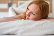 © ullision - Sexy serene redhead woman lies on a soft white bed, her face resting peacefully on her arms, exuding relaxation and warmth in a cozy, tranquil atmosphere