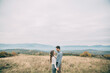 © Vasil - A couple standing in a field with mountains in the background. Scene is romantic and peaceful