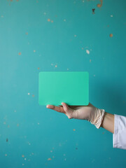 Poster - Doctor Holds Empty Green Card In Gloved Hand Against A Worn Blue Cement Wall With A Copy Space In The Foreground. 00001