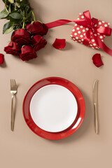 Wall Mural - Valentine's day table setting with white, red plate and red roses on beige background. View from above. Copy space. Romantic dinner for date. Vertical format.