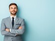 © JAKE STUDIO - A confident man in a gray suit stands with arms crossed against a light blue background, exuding professionalism and approachability.
