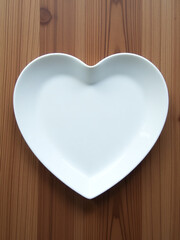Poster - A White Plate Shaped Like A Heart Is Placed On A Wooden Background Creating A Unique Table Setting. 00001