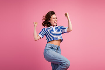 Wall Mural - Young woman with brown bob haircut celebrating on pink background wearing striped knitwear top and jeans