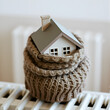 © Jennifer - House model in a woolen scarf. House figure wrapped in a warm scarf on a heater. Concept: warm house, heating, heat saving.