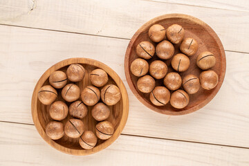 Wall Mural - Macadamia nuts in shell with wooden plate on wooden table, top view.