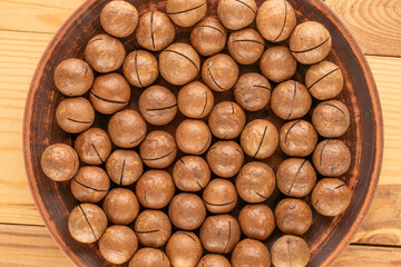 Wall Mural - Macadamia nuts in shell with clay plate on wooden table, top view.