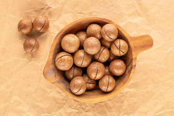 Wall Mural - Macadamia nuts in shell with wooden cup on kraft paper, top view.