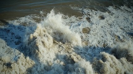 Poster - Aerial view of turbulent ocean waves crashing onto sandy beach with foam creating dynamic patterns in the water during daylight