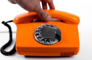 Bright orange rotary phone with a hand reaching for the receiver in a modern setting