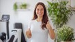 © Ketanoff - A young woman smiles confidently while giving a thumbs-up in a well-lit gym filled with plants. Her expression radiates determination and joy
