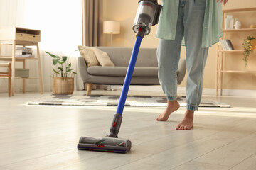 Woman cleaning floor with cordless vacuum cleaner at home, closeup