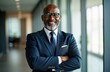 © Pete - Confident mid-aged African American businessman stands in office. Wears suit, glasses. Smiling, confident. Business leader in modern office. Professional manager executive. Successful business person