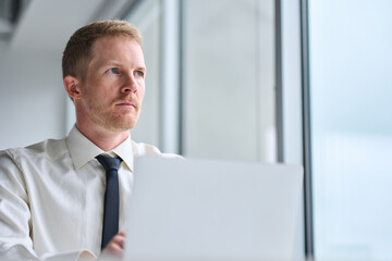 Wall Mural - Busy serious young business man executive, male investor looking away using laptop computer thinking on online project future financial growth strategy ideas working in office. Close up view