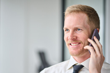 Wall Mural - Busy smiling professional business man manager, happy young male executive, businessman entrepreneur wearing tie talking on phone making call working in office looking through window. Close up photo.