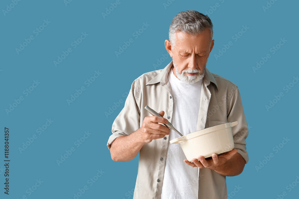 Mature man with spoon and cooking pot on blue background