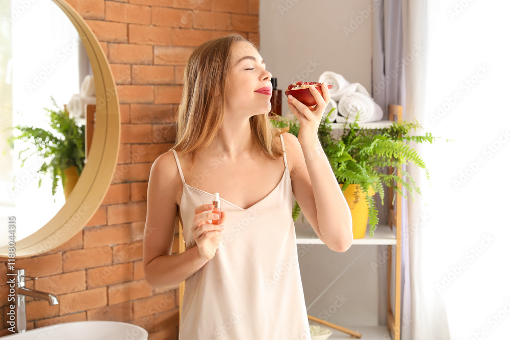 Young woman with pomegranate and serum in bathroom