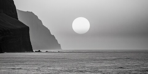 black and white photo of a large sun on the horizon over the ocean. the sky is cloudy and the sun is