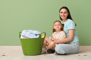 Wall Mural - Young woman and her little daughter with laundry basket near green wall at home