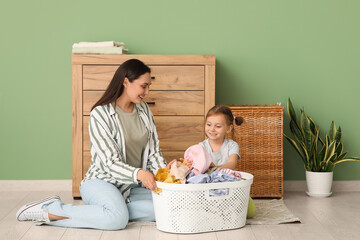 Wall Mural - Young woman and her daughter sort through fresh laundry near green wall at home