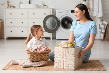 Wall Mural - Young woman and her little daughter with two baskets full of laundry at home