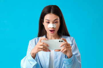 Wall Mural - Young woman with nose patch taking selfie on blue background