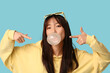 © Pixel-Shot - Pretty young Asian woman blowing bubble gum and pointing at it on blue background