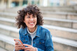 © Paula - Smiling woman wearing denim jacket holding phone outdoors