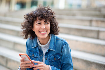 smiling woman wearing denim jacket holding phone outdoors
