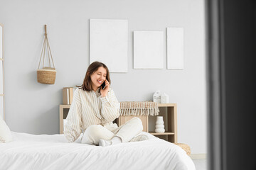 Wall Mural - Young woman talking by mobile phone near paintings on light wall in bedroom