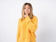© Jihan - Surprised Beautiful caucasian teen girl wearing orange sweater makes silence gesture, keeps finger over lips and looks mysterious at camera
