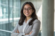 © Super Stocks - A photograph of an attractive young Indian woman in business attire, smiling with her arms crossed and standing confidently inside an office building.