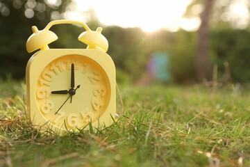 Wall Mural - Yellow alarm clock on green grass outdoors. Space for text