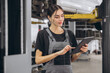 © anatoliycherkas - Young pretty smiling female mechanic, in grey uniform, holding tablet in her hands, poses standing under car on lift.